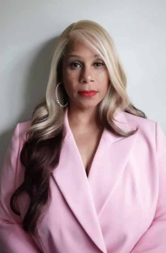 Woman with long blonde hair wearing a pink blazer.