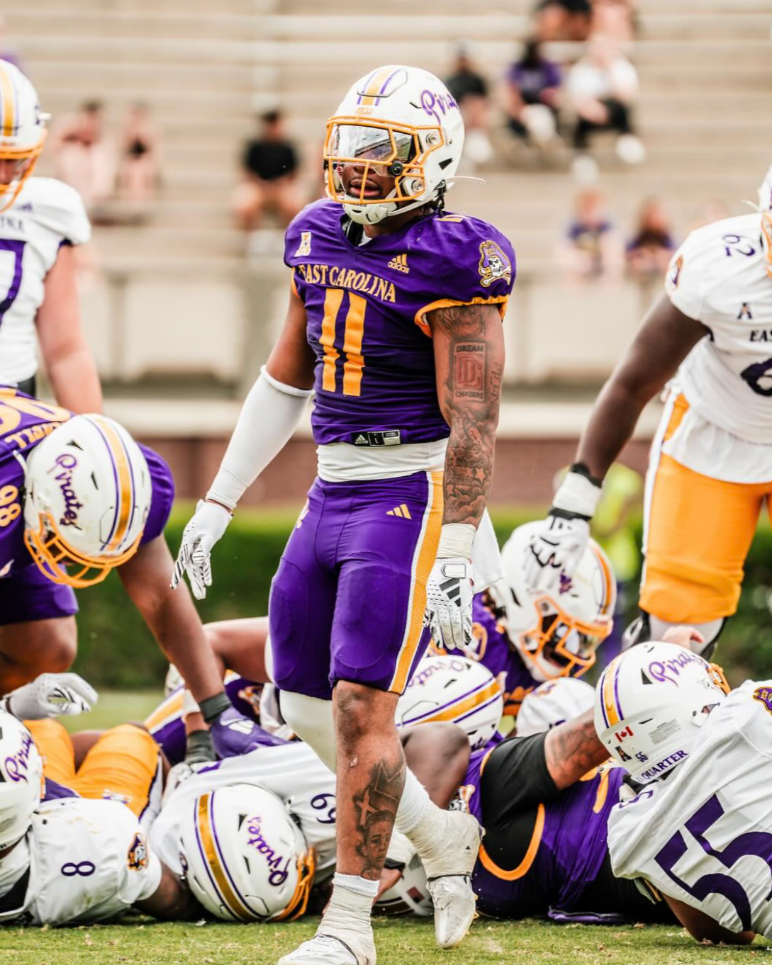 Football player in purple uniform standing amid a group on the field.
