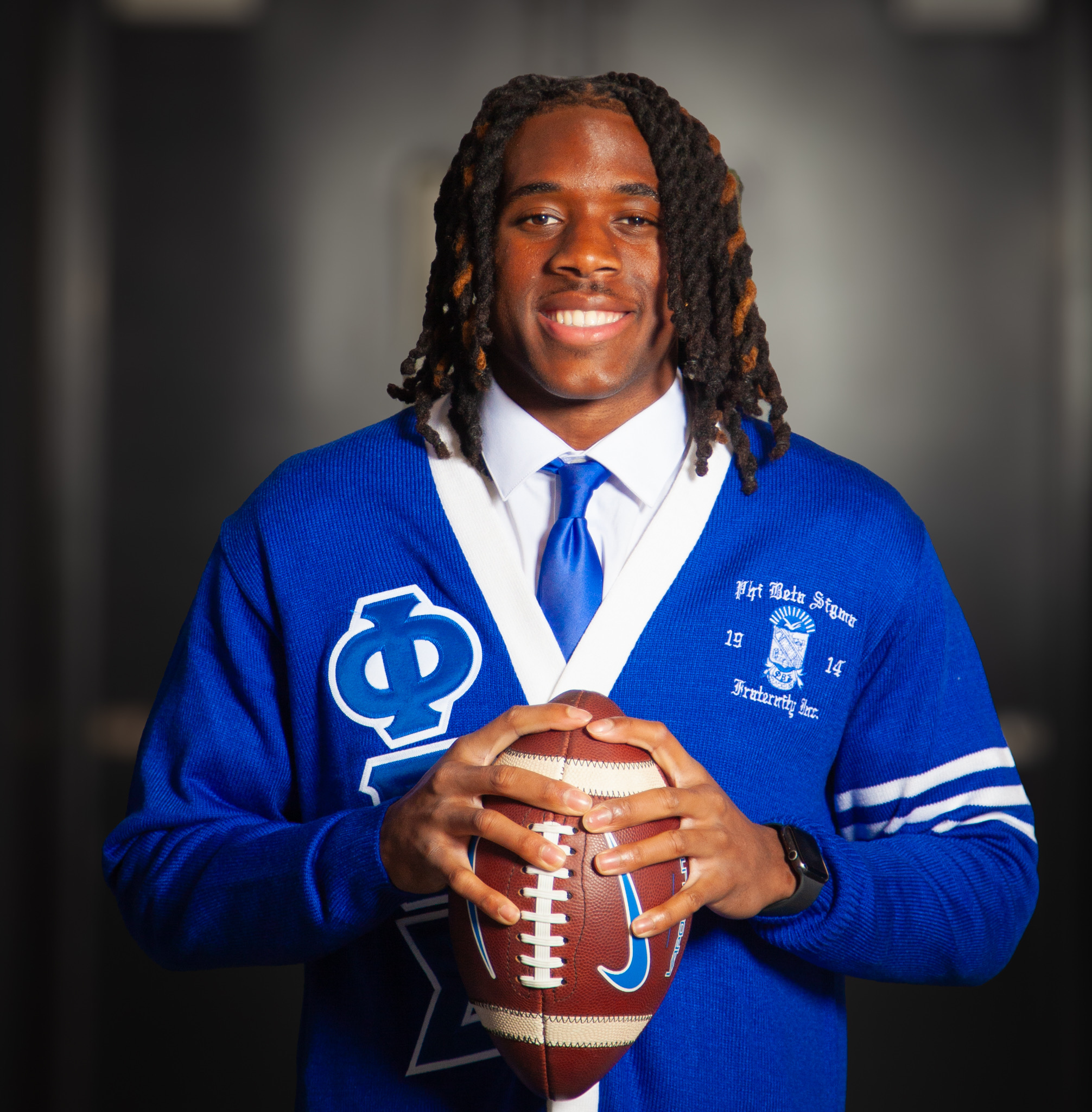 Smiling young man in a blue fraternity sweater holding a football.